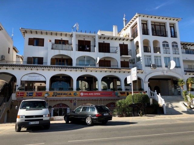 Knappt 10 minuters promenad från lägenheten ligger Villamartín Plaza. Här finns ca 20-25 restauranger i tre plan med varierande utbud. Finns det barn med i sällskapet föreslår jag en av restaurangerna en halv trappa ner. Här kan barnen springa helt fritt på torget medan föräldrarna äter färdigt i lugn och ro. Här finns flera mindre butiker, mäklarföretag och en bank med bankomat, Caixa Bank. I souterrängplan utmed gatan, ligger en mindre livsmedels-butik som har det mesta. Manuell chark, frukt o grönt, mejeriprodukter, kemisk-tekniska produkter och givetvisl vin, öl och även starkare drycker för de som önskar köpa sådant. Under högsäsong är butiken öppen alla dagar i veckan med mycket generösa öppettider. Entrén är rakt under 